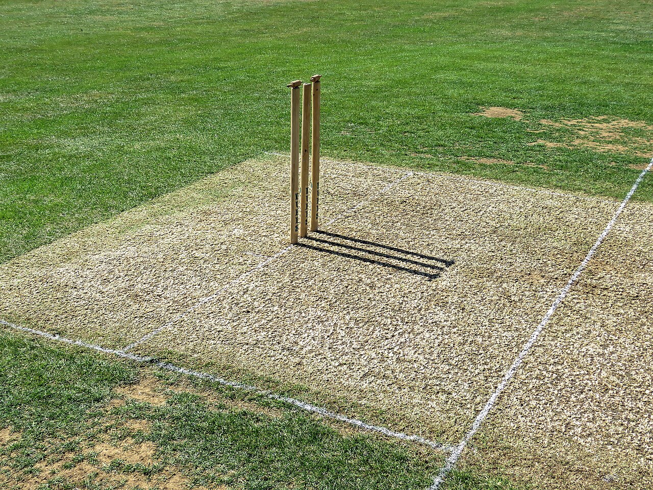 FairPlay Gujarat Cricket Pitches: stumps and a red ball on a prepared strip in a floodlit ground